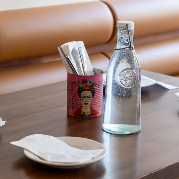 A table setting with a water bottle, a Frida Kahlo-themed utensil holder, and a plate with a napkin.