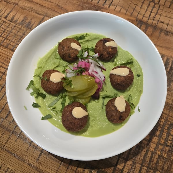 El Cedro's falafel with green hummus, pickled vegetables, and tahini drizzle on a white plate.