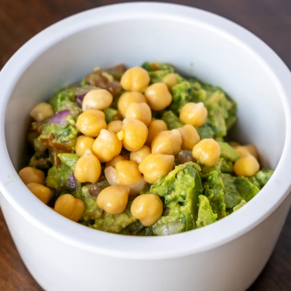 A white bowl filled with green guacamole topped with whole chickpeas and red onion.