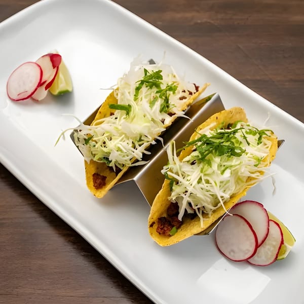 Two tacos with shredded cabbage and cilantro, served with radish slices and lime wedges on a white plate.