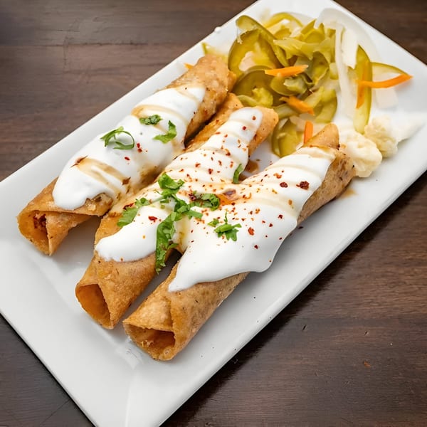 Three crispy Lebanese flautas topped with white sauce, herbs, and chili flakes, served with pickled vegetables.